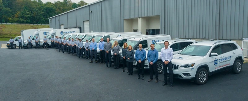 Camelot Restoration team standing in front of their fleet of service vans and trucks