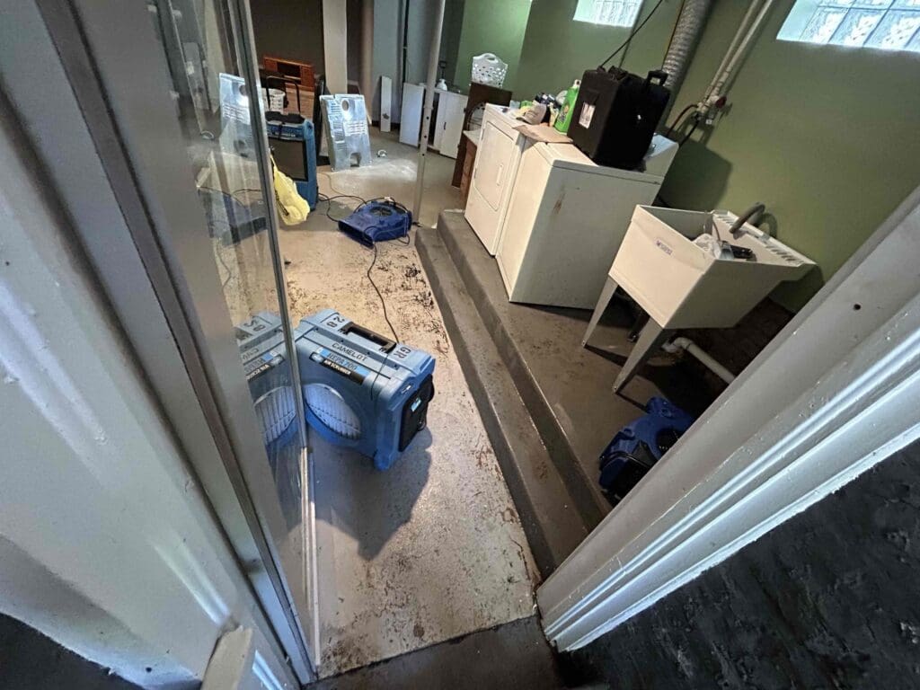 A dehumidifier drying a laundry room with a washer and utility sink after an appliance leak