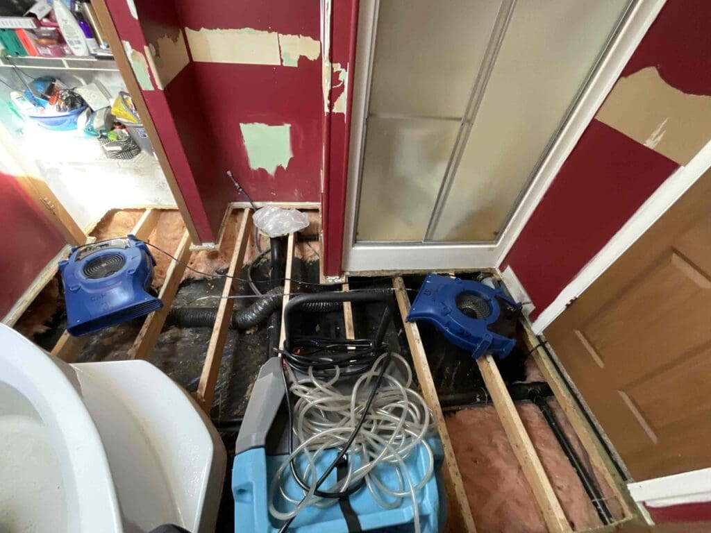 Air movers and a dehumidifier drying exposed bathroom floor joists