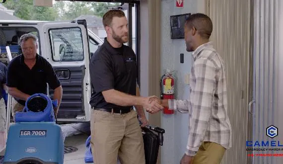 Camelot technician shaking hands with a homeowner beside a service van and a dehumidifier, shown for Kalamazoo
